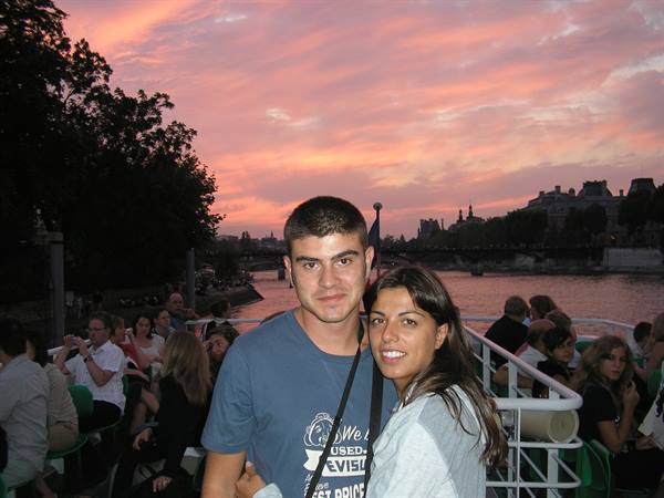 Smiling couple on Seine river boat, pink evening sky, Paris