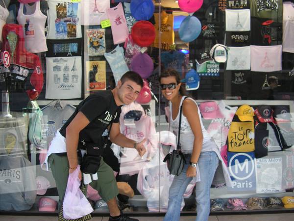 Smiling tourists in front of a Paris souvenir shop with shirts and caps