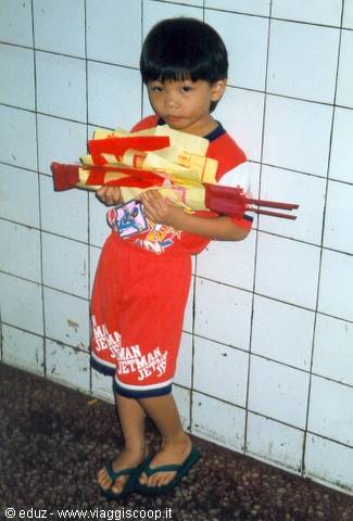 Boy in red shirt and flip-flops holding paper toys against white tiled wall
