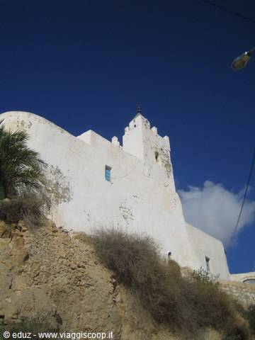 white fortified mosque on rock, blue sky, dry bushes