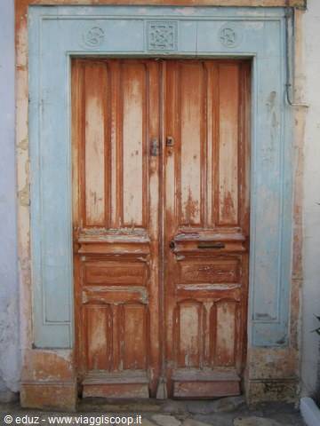 Weathered double wooden door framed by faded pale blue plaster
