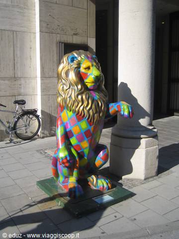 Lion statue painted with colorful checkered patterns beside a stone column, bicycle nearby