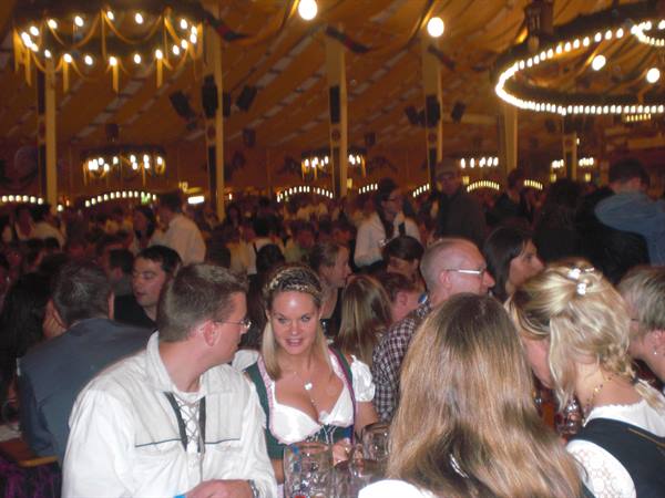 Women in dirndls among crowd and lights inside the Oktoberfest tent