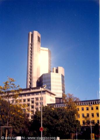 Glass and concrete skyscraper above low buildings under a blue sky