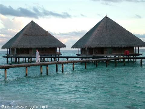 Thatched wooden stilt bungalows over lagoon, man walks along wooden jetty