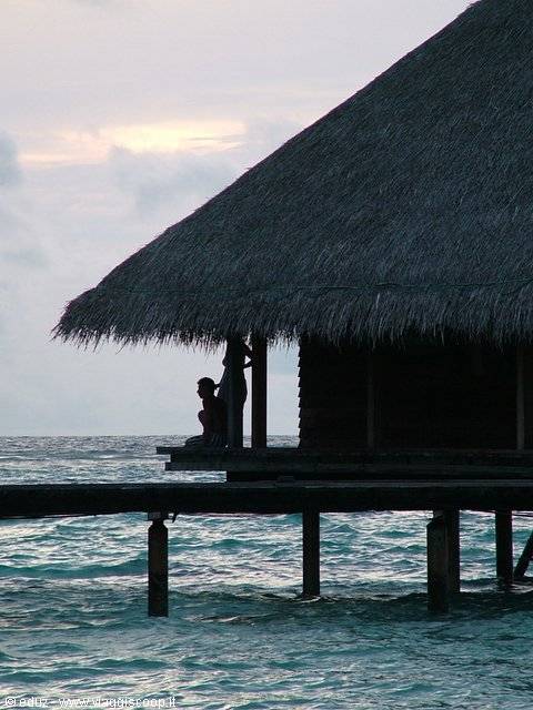 Thatched overwater bungalow on stilts, silhouettes at dusk above the sea