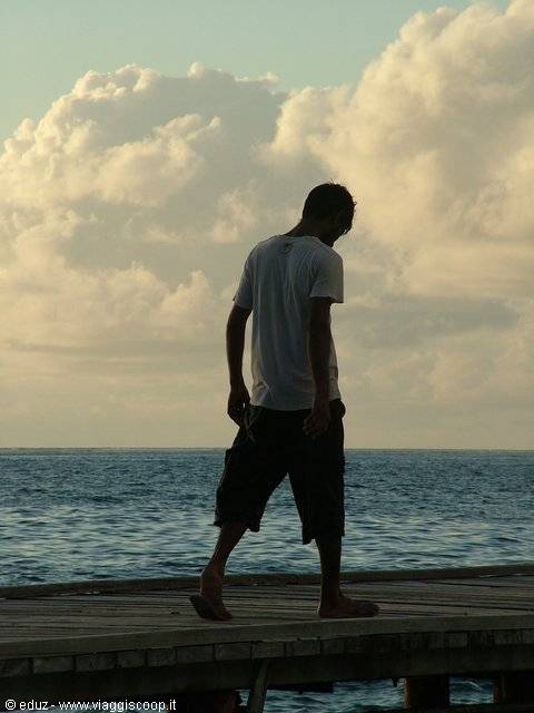 Man walks barefoot on the wooden pier in front of the sea