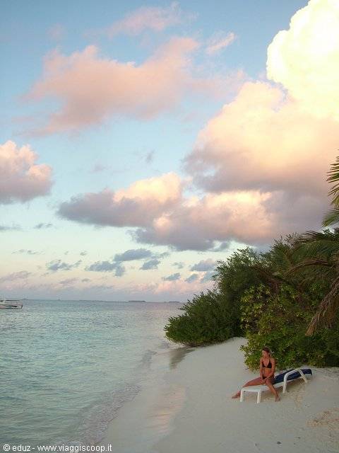 Woman on white sun lounger in the sand, palms and pink clouds at dusk
