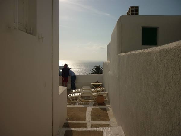 Tourists on a whitewashed terrace with sun loungers gaze at the sea