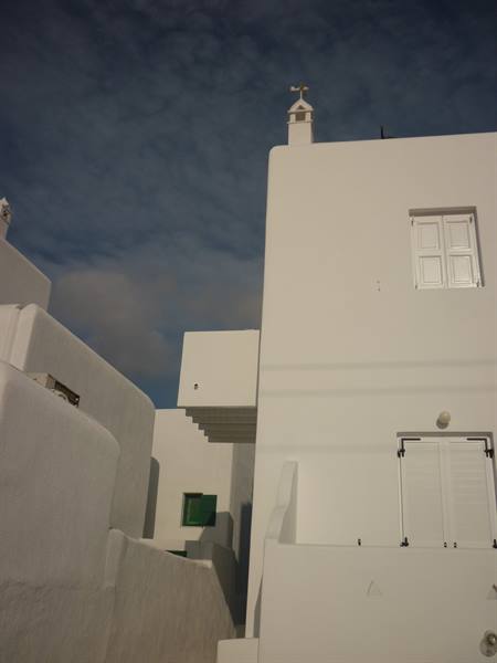 Whitewashed Cycladic houses with traditional chimney and shutters under cloudy sky