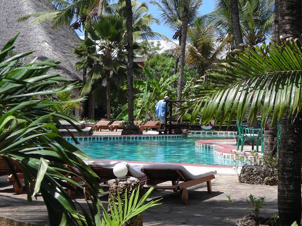 Pool surrounded by palms and wooden loungers at a thatched-roof resort