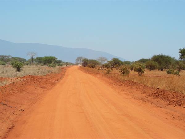 Red dirt road through dry bushes, blue mountains under clear sky