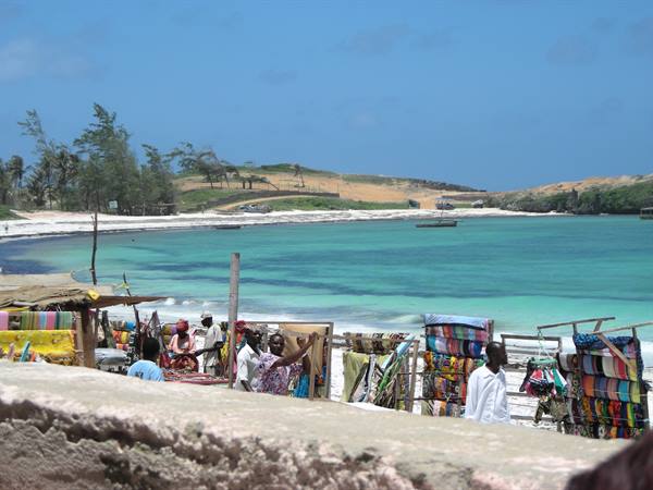 Colorful fabric market stalls on the beach, turquoise sea with boats