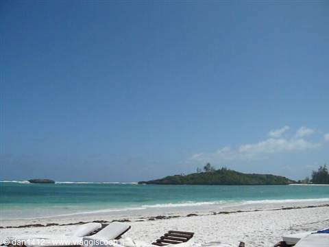 White sand beach with empty loungers and a green islet on turquoise sea