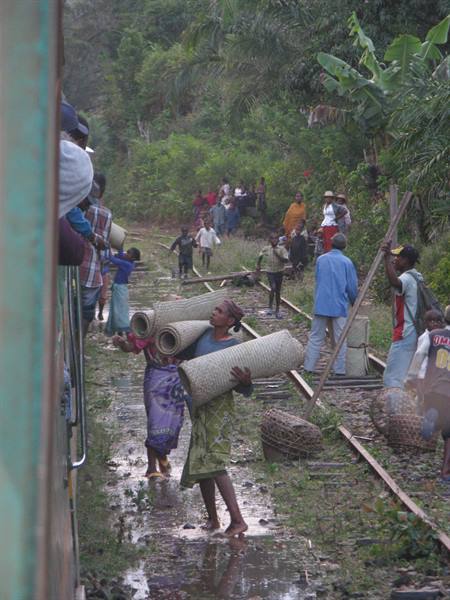 Women on muddy railway tracks sell woven mats to train passengers