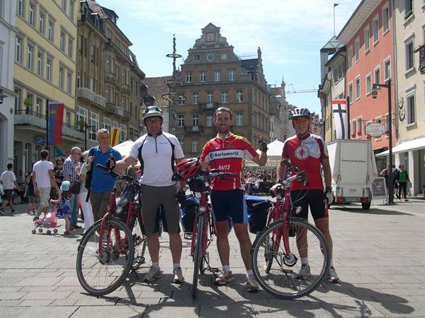 Three cyclists with red bicycles in a pedestrian square among colorful buildings
