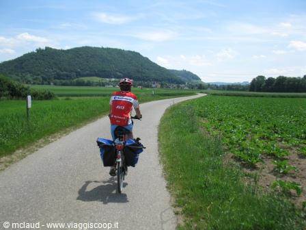 cyclist with panniers rides on gravel road between cultivated fields and hills