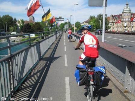 Touring cyclist with panniers crosses a steel bridge lined with flags