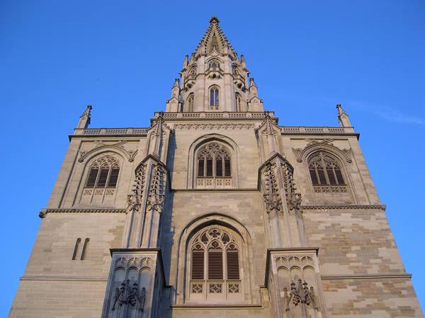 Stone facade of a neo-Gothic church with spire, lit by sunlight