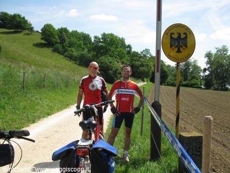 Two cyclists in red jerseys at the German border with loaded bikes