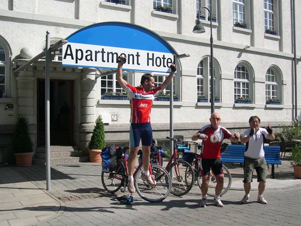 Cyclists celebrating on their bikes in front of an apartment hotel sign