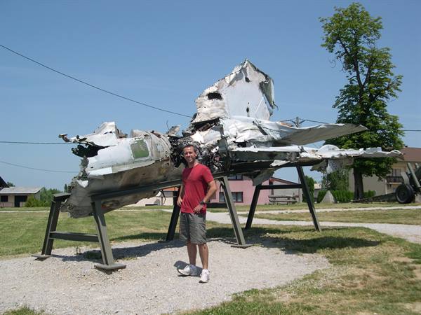 Tourist posing beside a wrecked fighter jet mounted on metal stands