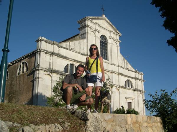 couple with dog before a white stone church facade, blue sky, strong sunlight
