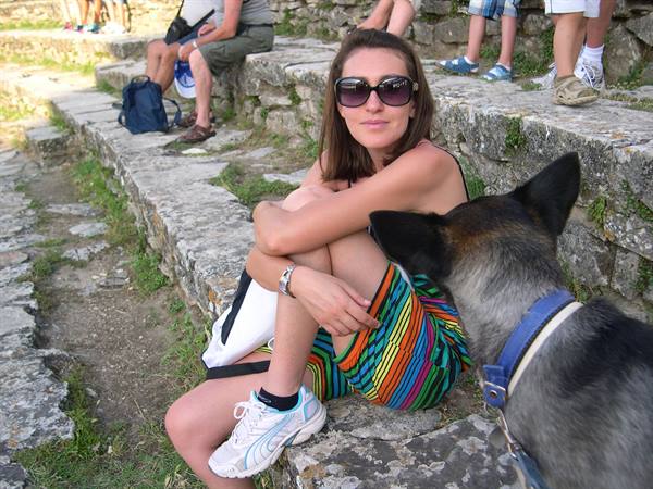 Woman in sunglasses sitting on ancient stone steps, a dog sniffing her