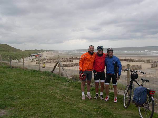 Three cyclists in colorful jackets posing on grass above the beach dunes