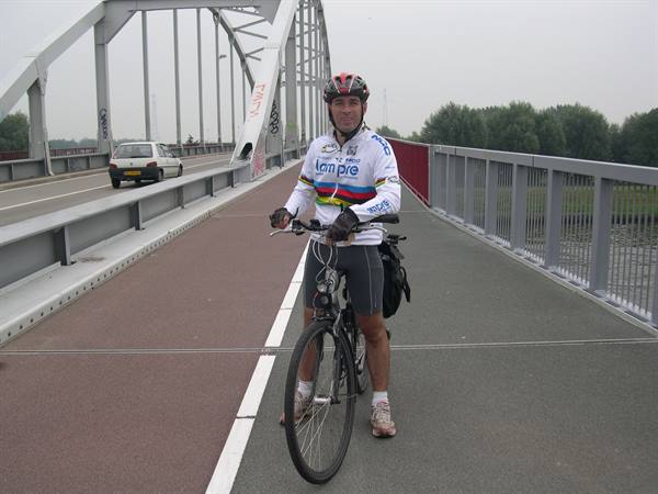 Cyclist in helmet and cycling jersey standing with bike on a steel arch bridge path
