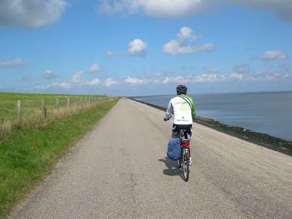 Cyclist with blue pannier rides gravel road between dike and sea