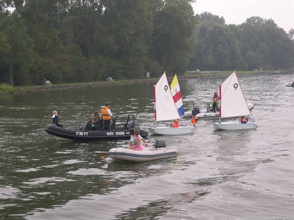 Inflatables and small sailboats with children on water, misty trees behind