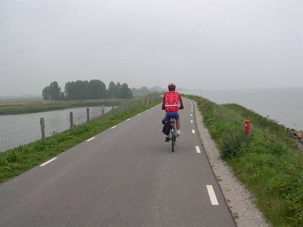 Cyclist in red jersey on a causeway road between two waters, grey day