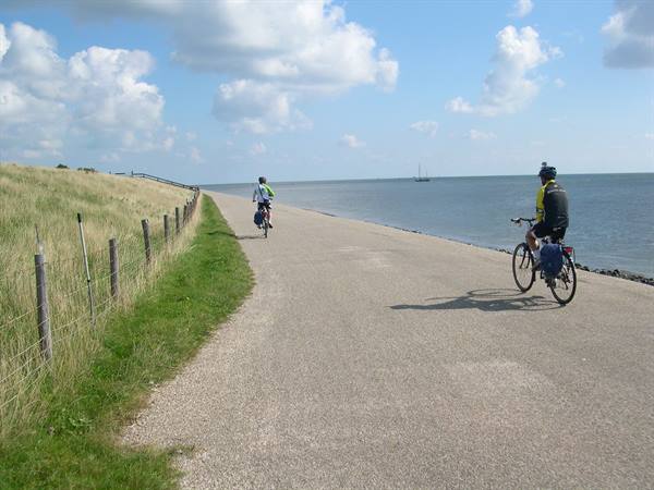 Cyclists with touring panniers ride along a paved dike beside the sea