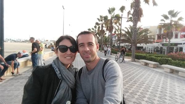 Couple taking selfie on palm-lined seaside promenade with tiled pavement
