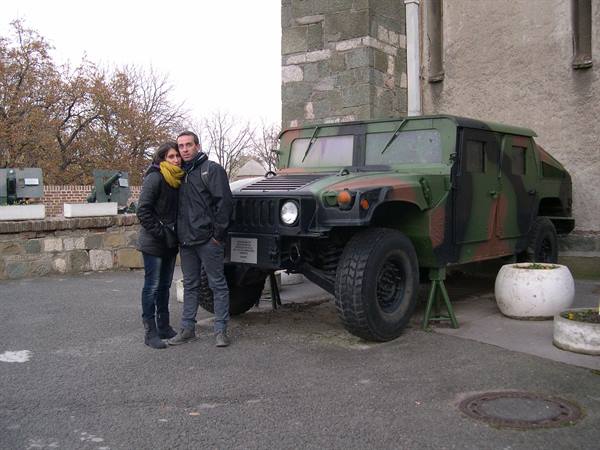 couple beside camouflaged military Humvee on concrete, gray sky