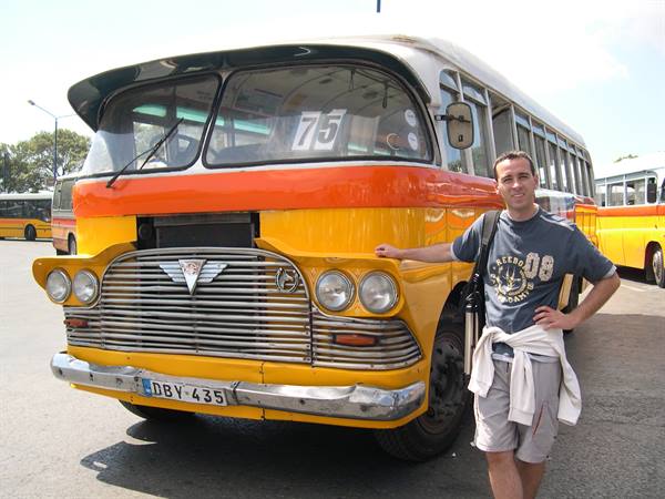 Tourist beside a vintage yellow and orange Maltese bus