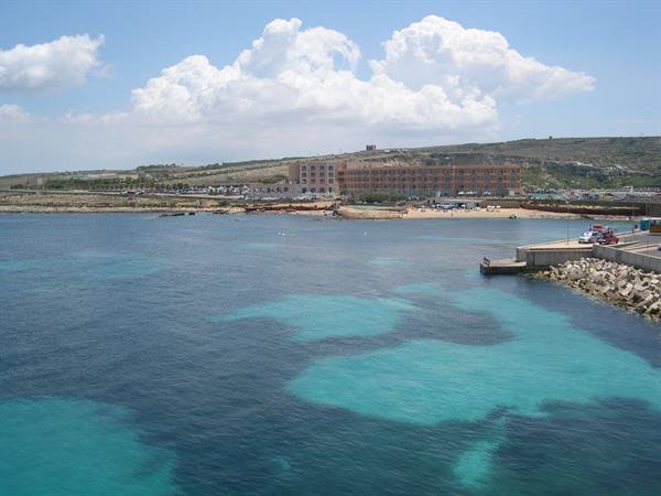 Turquoise waters in front of a hotel and concrete pier at Ċirkewwa, Malta