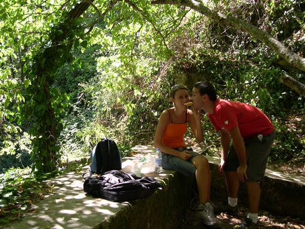 Woman sitting on a stone wall next to backpack, man kisses her cheek
