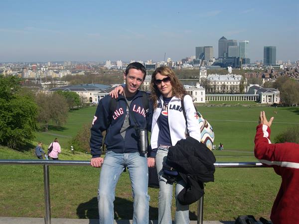 Couple leaning on a railing in Greenwich, with Canary Wharf and the Queen's House behind