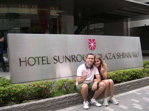 Couple crouching with peace signs in front of Hotel Sunroute Plaza Shinjuku metal sign