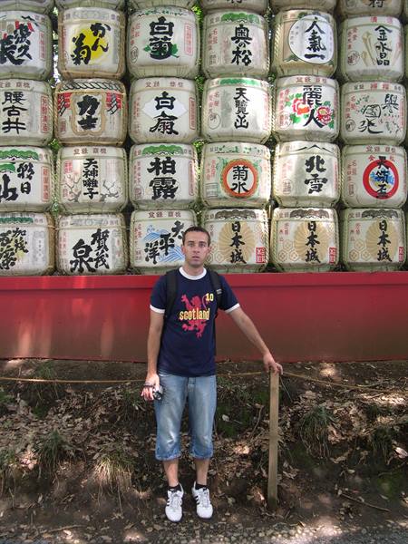 Tourist in blue shirt standing before a wall of decorated sake barrels