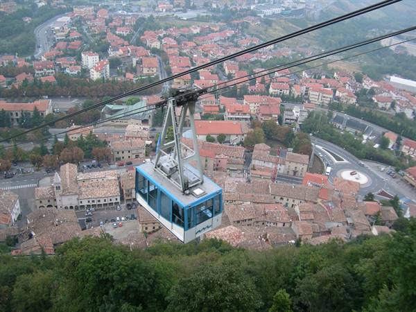 Blue cable car over San Marino rooftops, cables and hazy town below