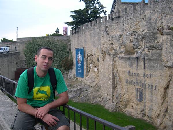 Young man in green shirt and backpack beside Avignon's medieval stone walls