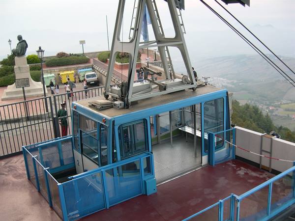 Blue cable car cabin at San Marino's upper station, misty hills beyond