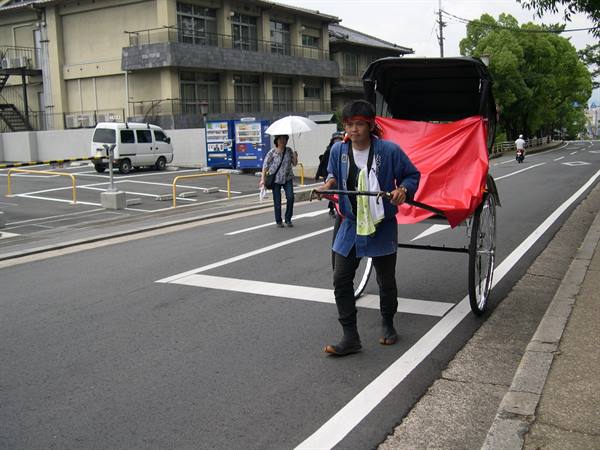 Rickshaw puller in blue jacket walking on a city street with red canopy