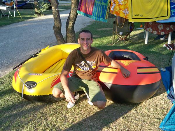 Young man crouching between a yellow dinghy and an orange tube at the campsite