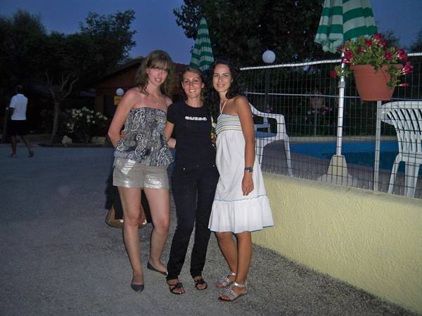 Three friends posing by the pool, green umbrellas in evening light