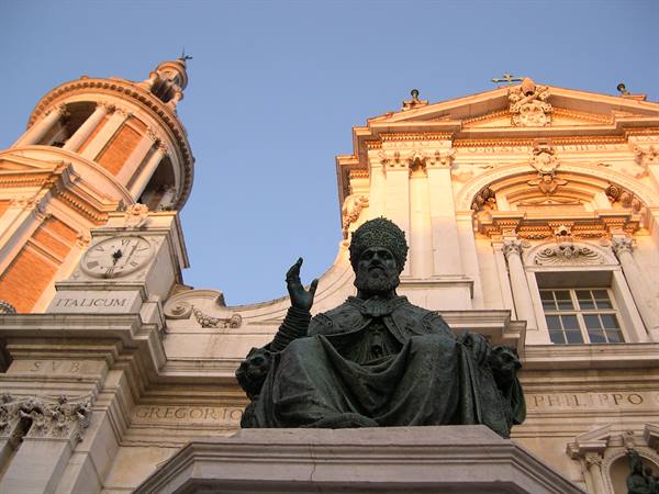 Bronze statue of seated pope before baroque church facade at sunset
