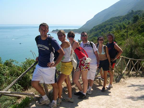 Group of hikers posing on dirt trail with wooden fence, blue sea behind